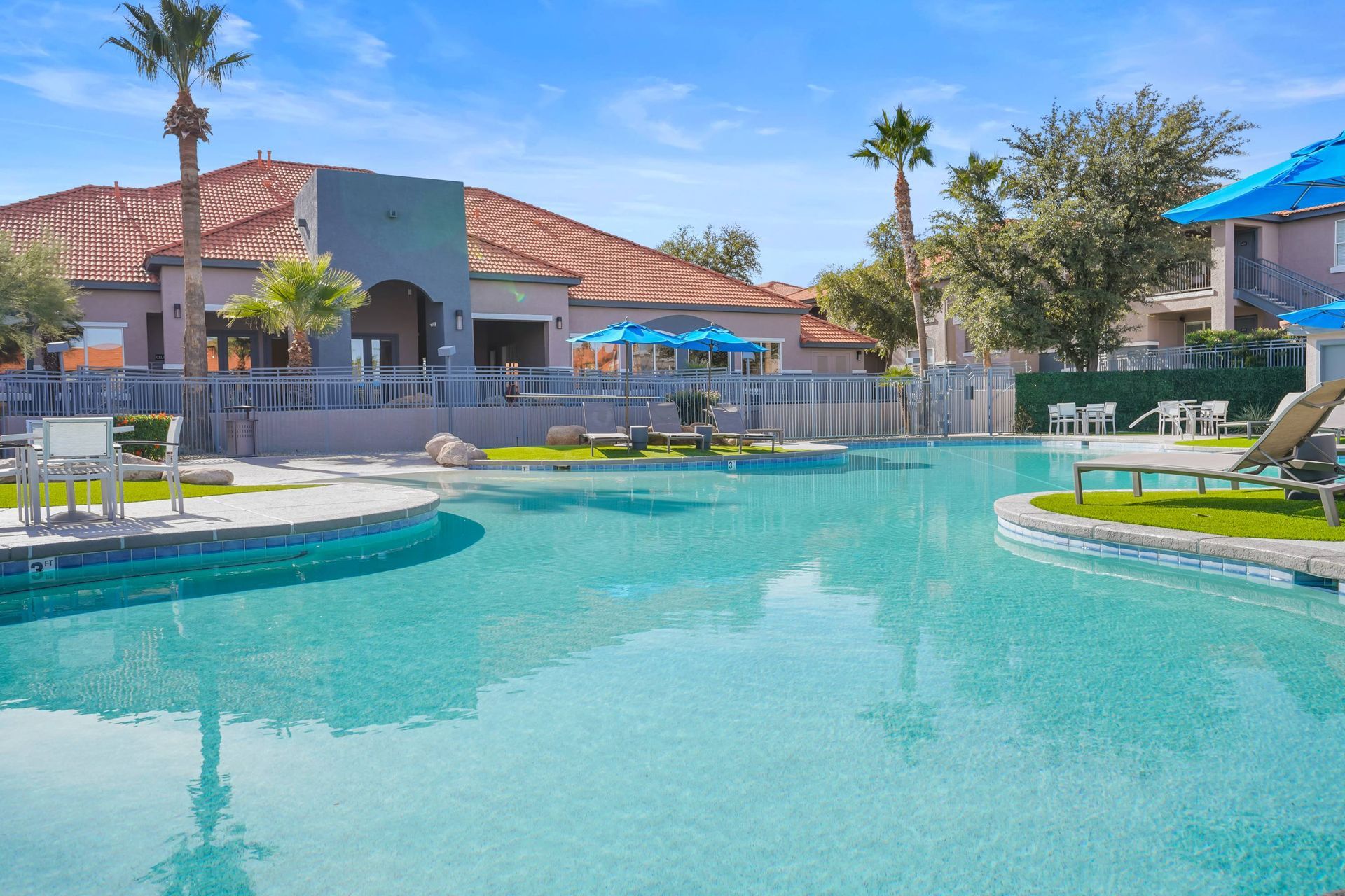 Outdoor pool at a multifamily community with lounge chairs and blue umbrellas.