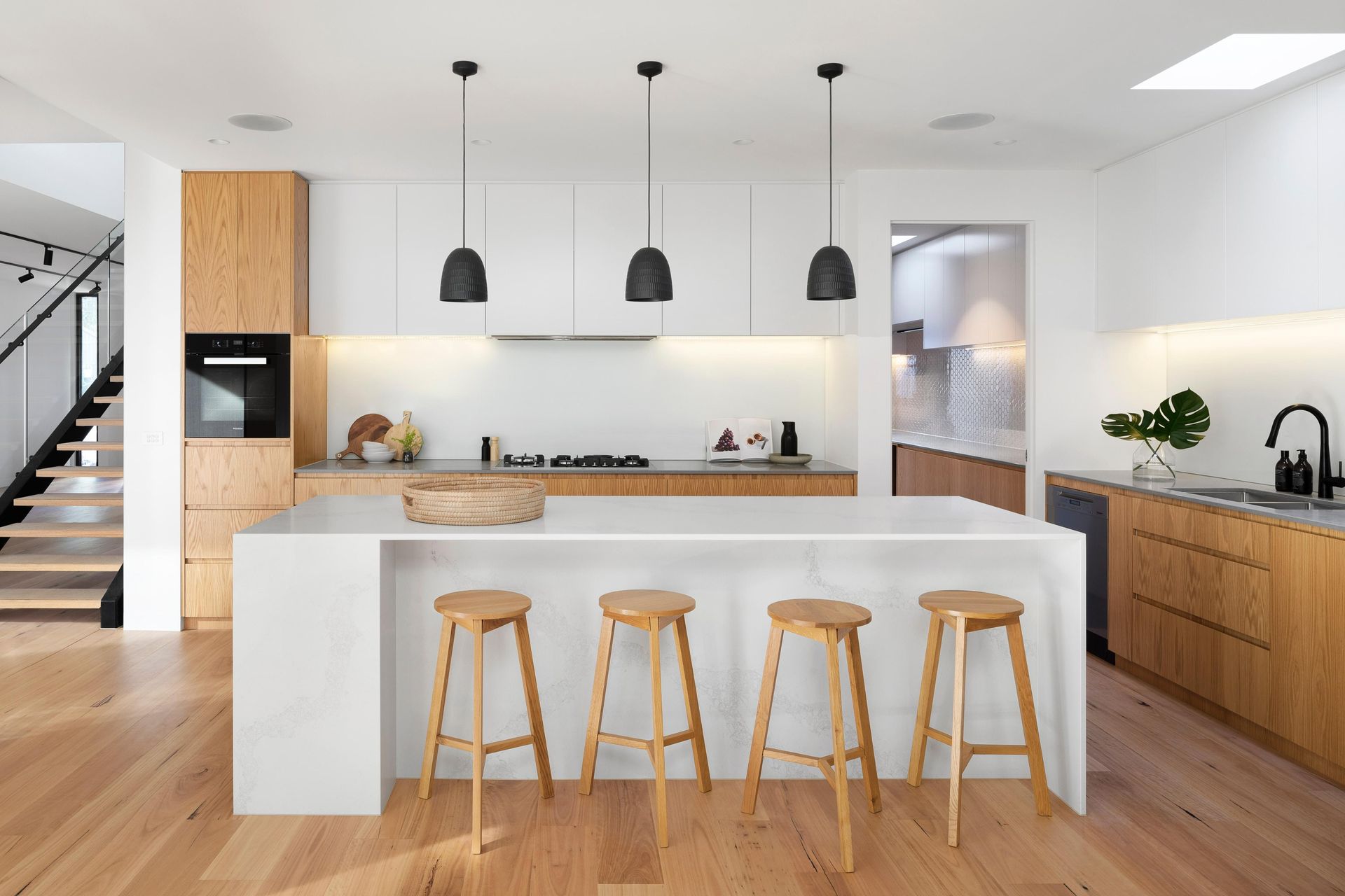 Modern kitchen with light wood cabinets, white countertops, island with stools, and black pendant lights.