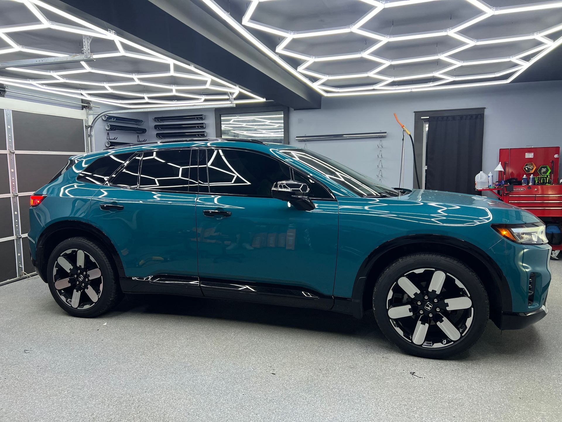 A white sports car is parked in a garage under a honeycomb ceiling.