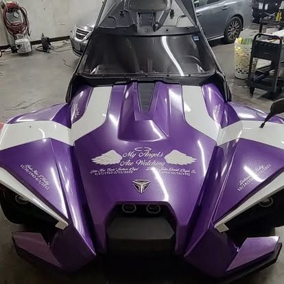 Purple and white three-wheeled vehicle with angel wing decals, parked indoors.