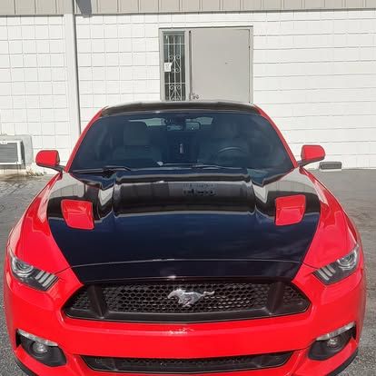 Red Ford Mustang with a black hood parked in front of a white building.