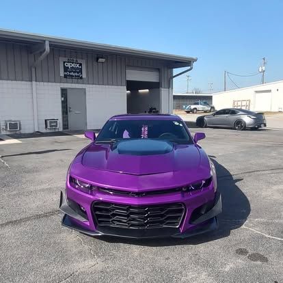 Purple Chevrolet Camaro parked outside a building, another car visible in the background.