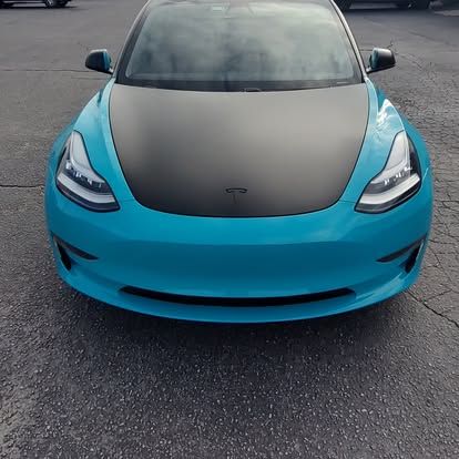 A teal Tesla with a black hood parked on asphalt.
