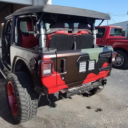 A customized camouflage-painted Jeep Wrangler with red accents, large tires, and an open top.