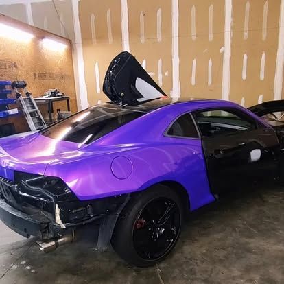 Purple and black car with the door and rear panels removed in a workshop.