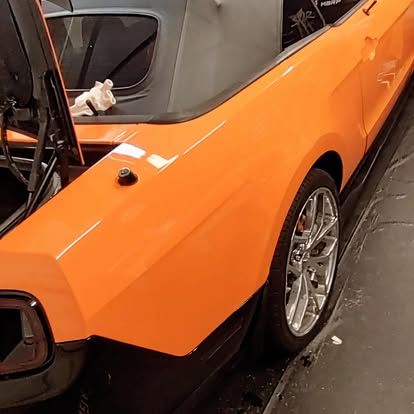 Orange convertible car with black accents and chrome wheels; hood open.