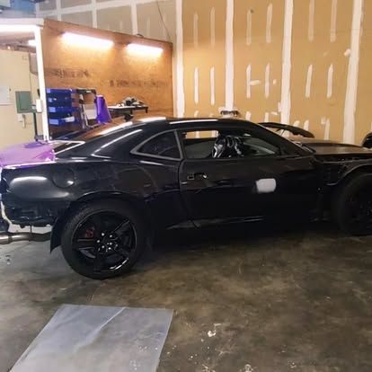Black Camaro car in a garage, undergoing repairs, with purple visible in the rear.