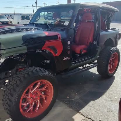 Custom Jeep Wrangler with red accents, camouflage hood, and large orange wheels.