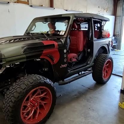 Modified Jeep Wrangler with red accents, large tires, in a garage.
