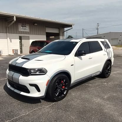 White Dodge Durango with gray racing stripes parked in front of a building on a sunny day.