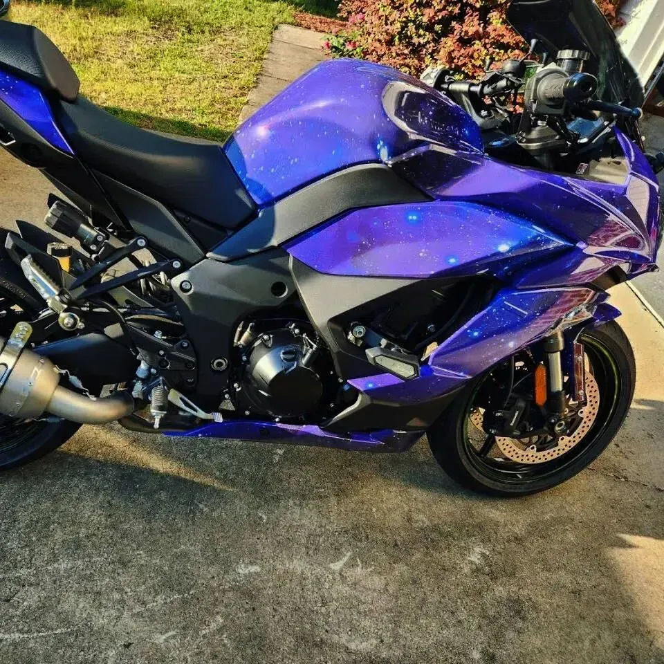 A Kawasaki motorcycle with a purple galaxy paint scheme parked on a concrete surface.