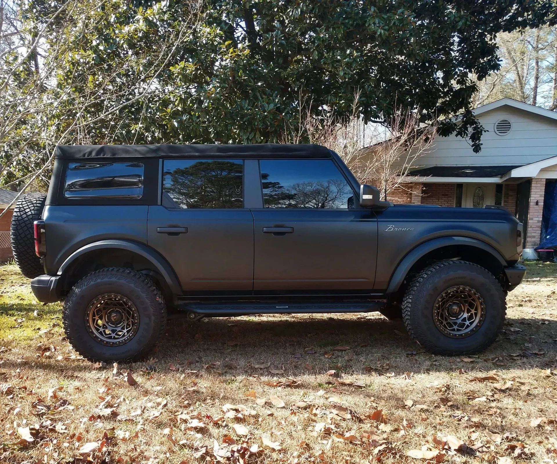 Black Ford Bronco SUV with dark bronze wheels parked on dry grass.