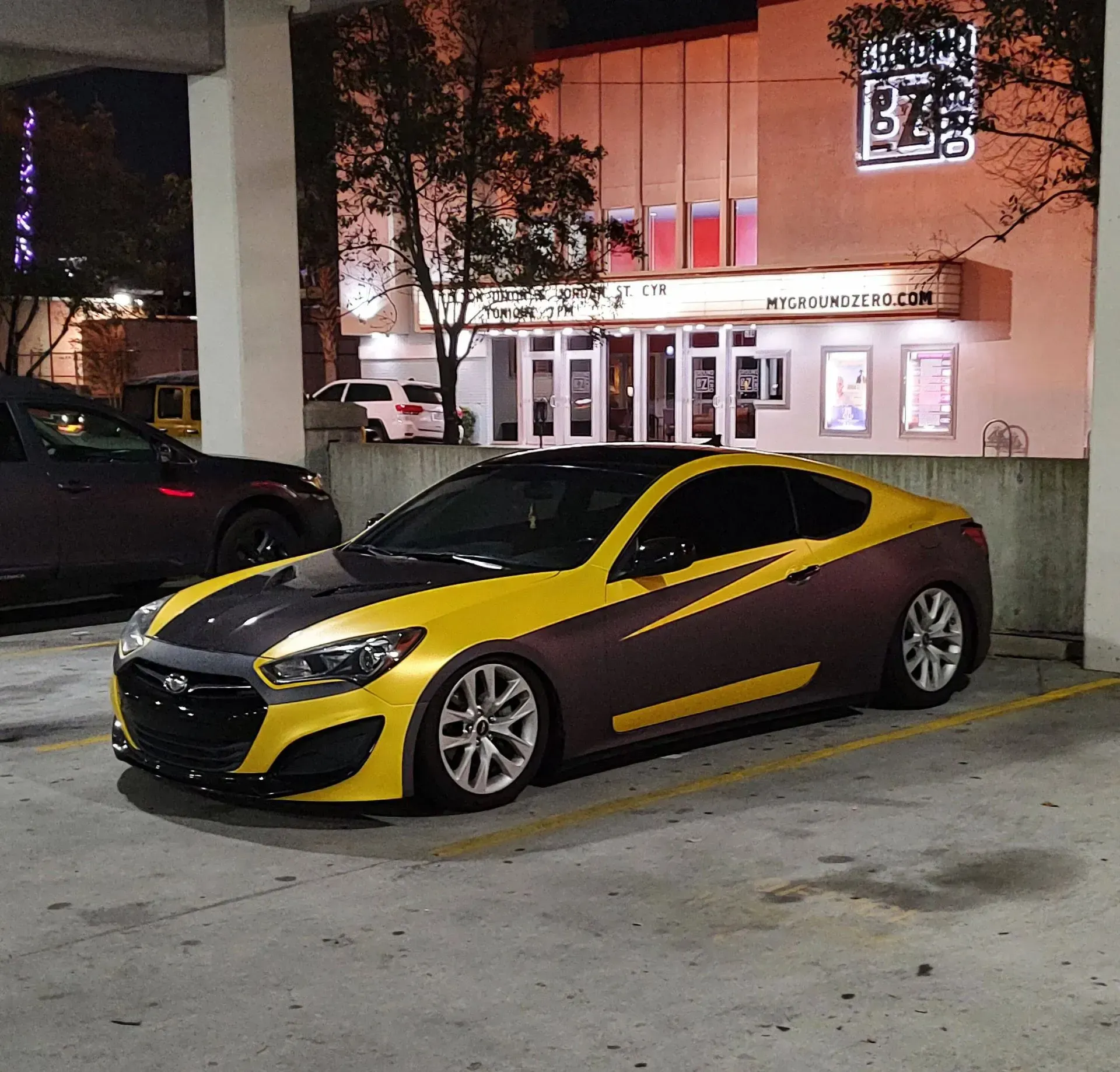 Yellow and brown customized car parked in front of a building at night.
