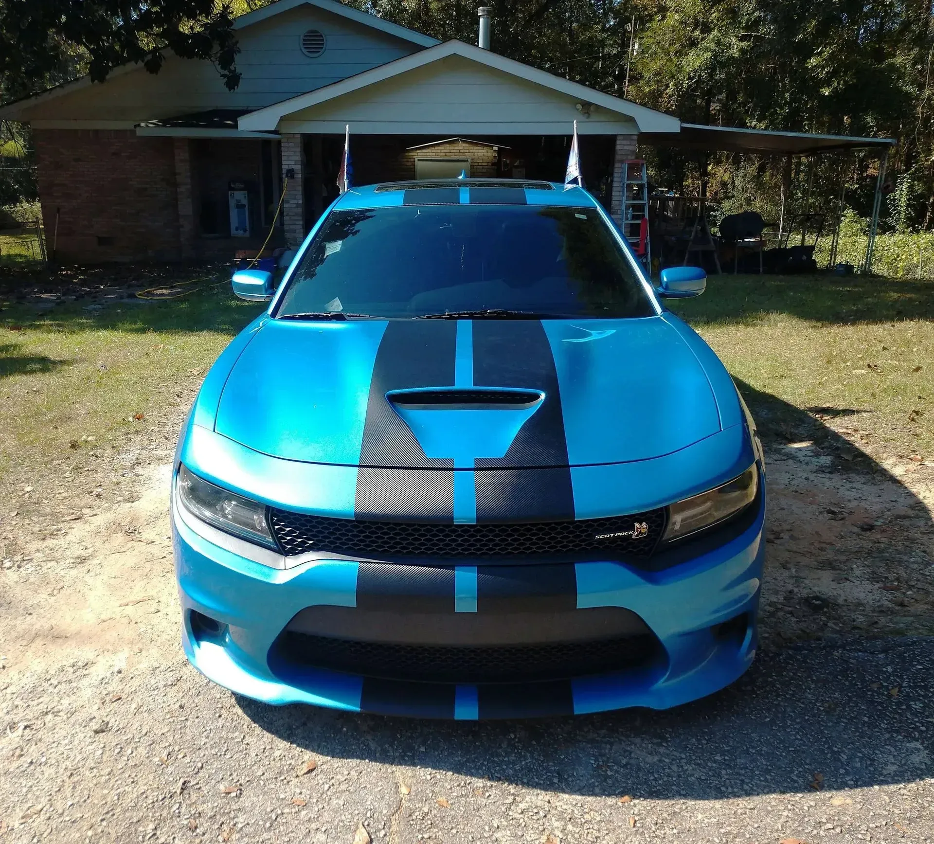 Blue Dodge Charger with black racing stripes parked in front of a house.