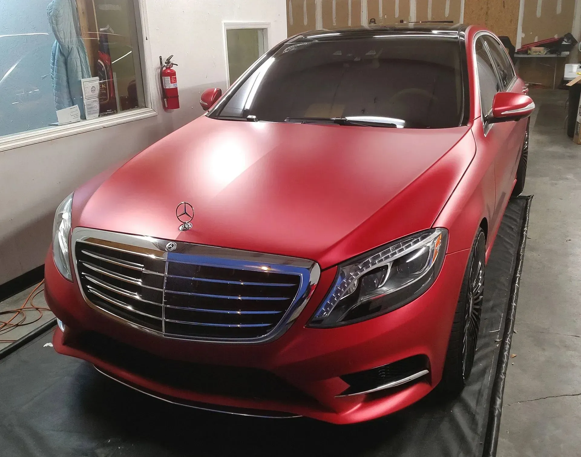Red matte-finished Mercedes-Benz sedan in a garage, black roof, and chrome accents.