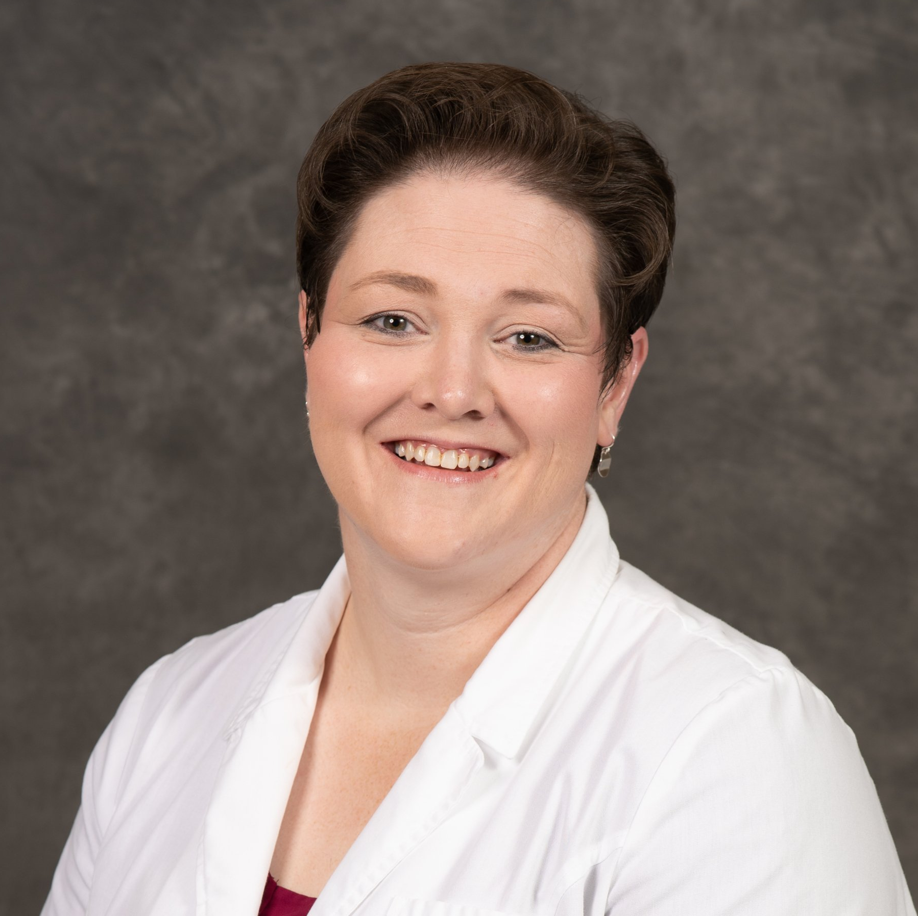 A woman in a white lab coat is smiling for the camera.