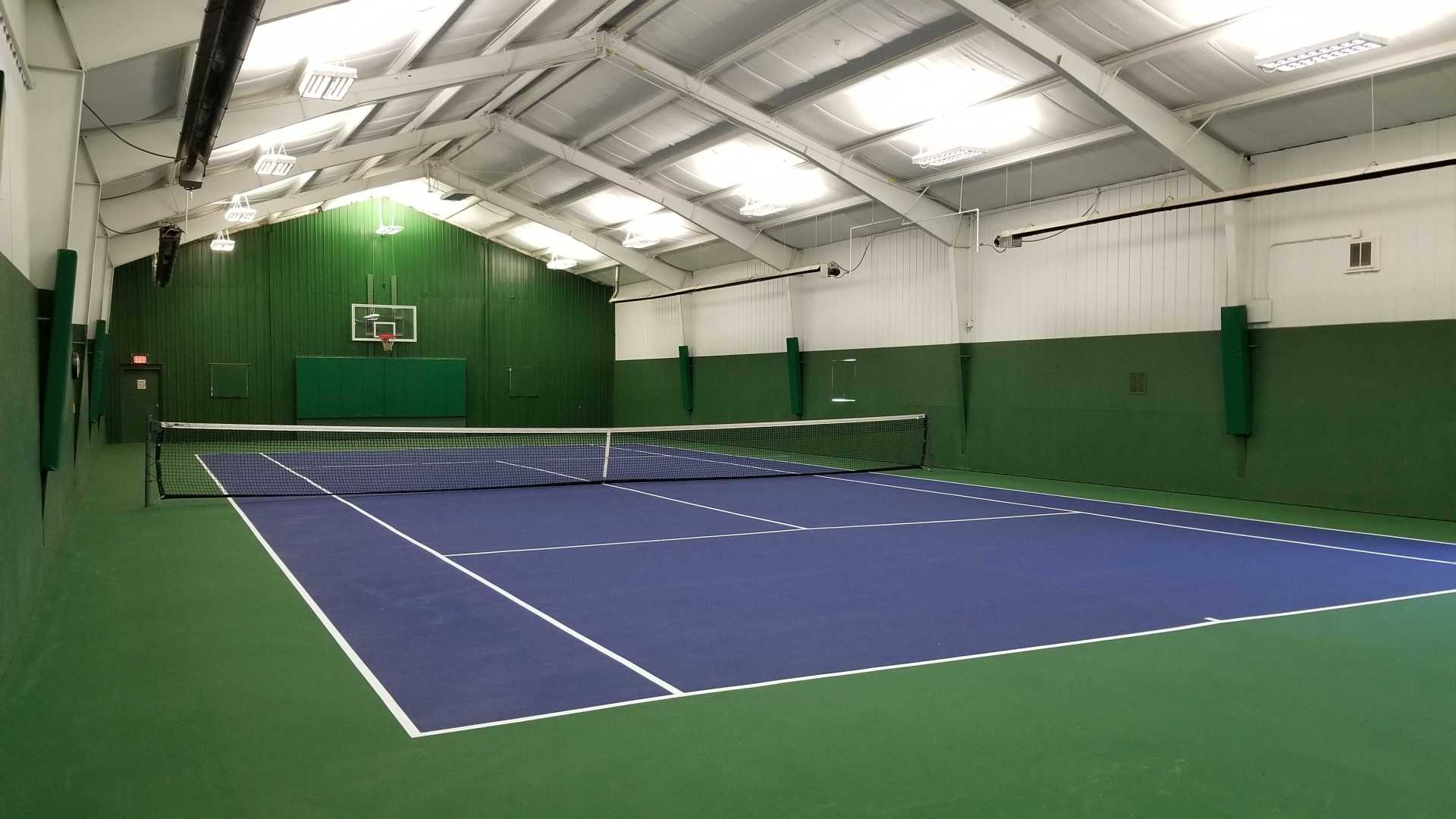 an indoor tennis court with a basketball hoop in the background