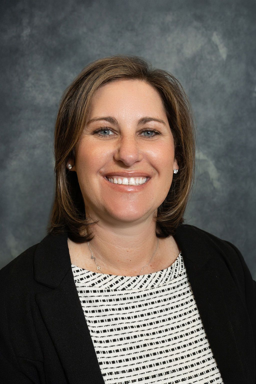 A woman in a black jacket and white shirt is smiling for the camera.