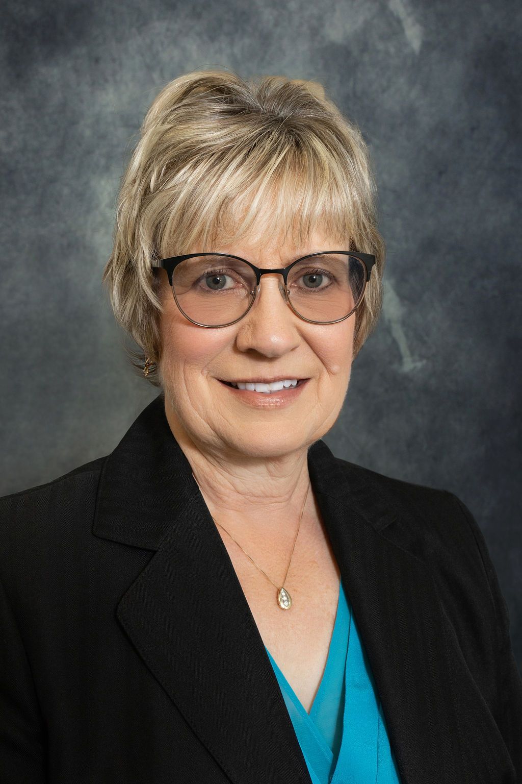 A woman wearing glasses and a black jacket is smiling for the camera.