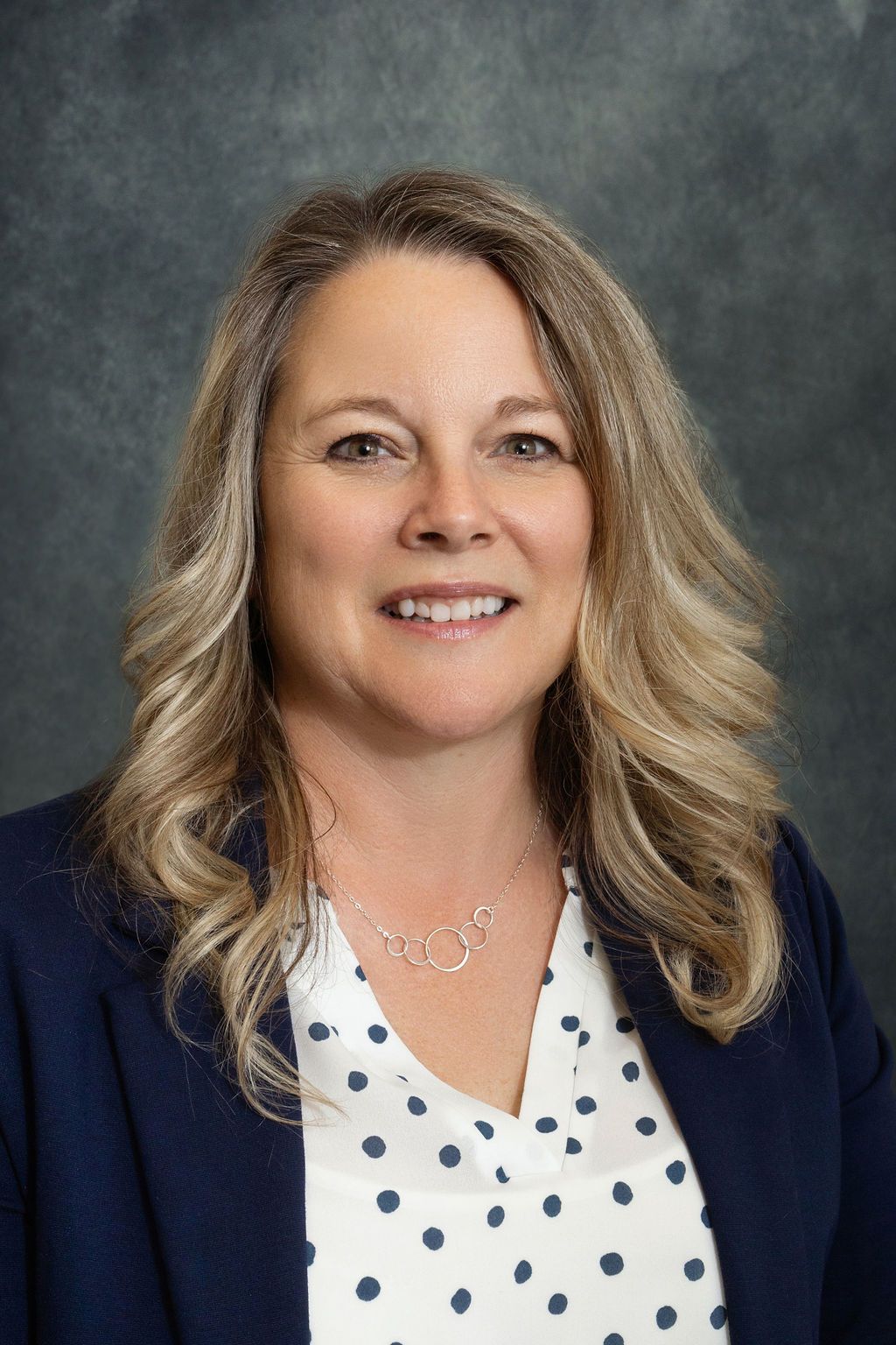A woman in a blue jacket and white polka dot shirt is smiling for the camera.