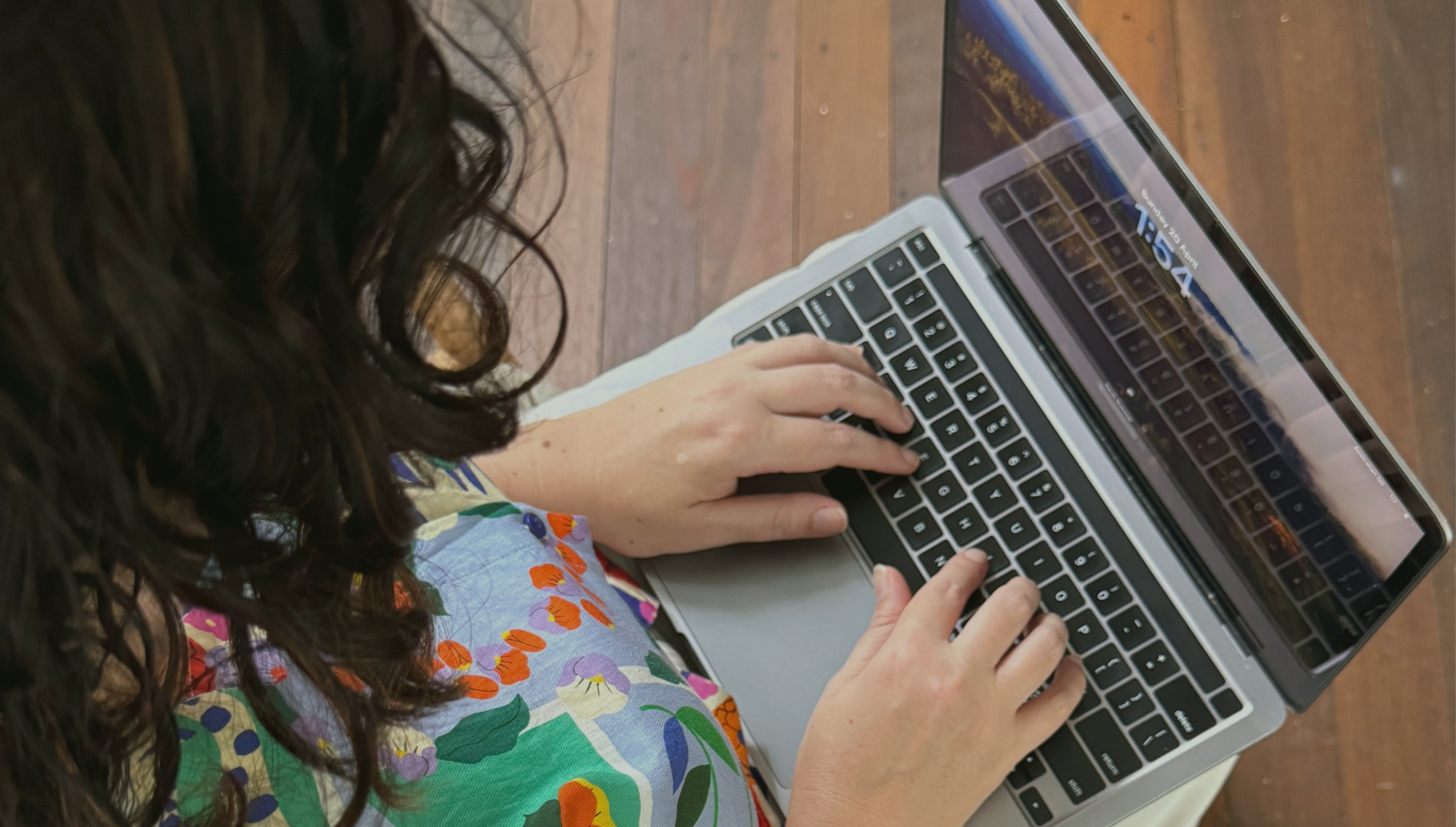 A woman is typing on a laptop computer on a wooden table.