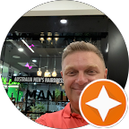 A man in a red shirt is smiling in front of a store.