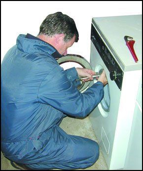  man in blue overall fixing a white washingmachine