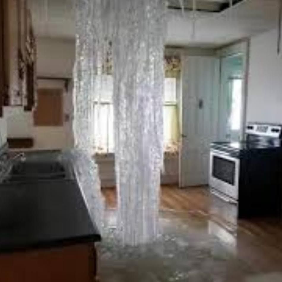 Kitchen with water gushing from the ceiling, causing flooding and damage.