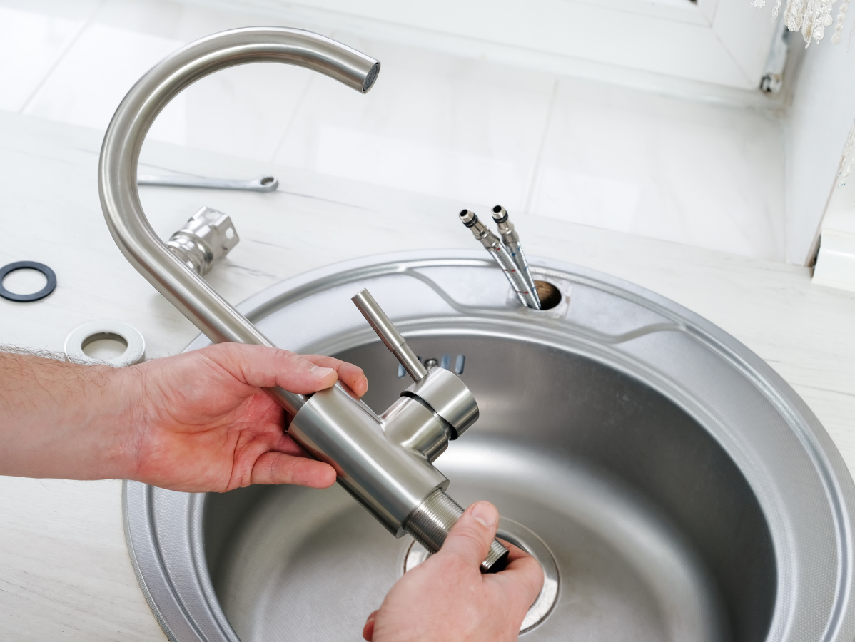 Hands installing a new stainless steel kitchen faucet into a sink.