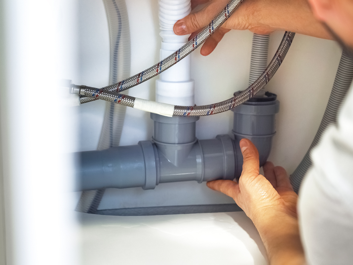 Hands connecting gray plumbing pipes under a white sink.