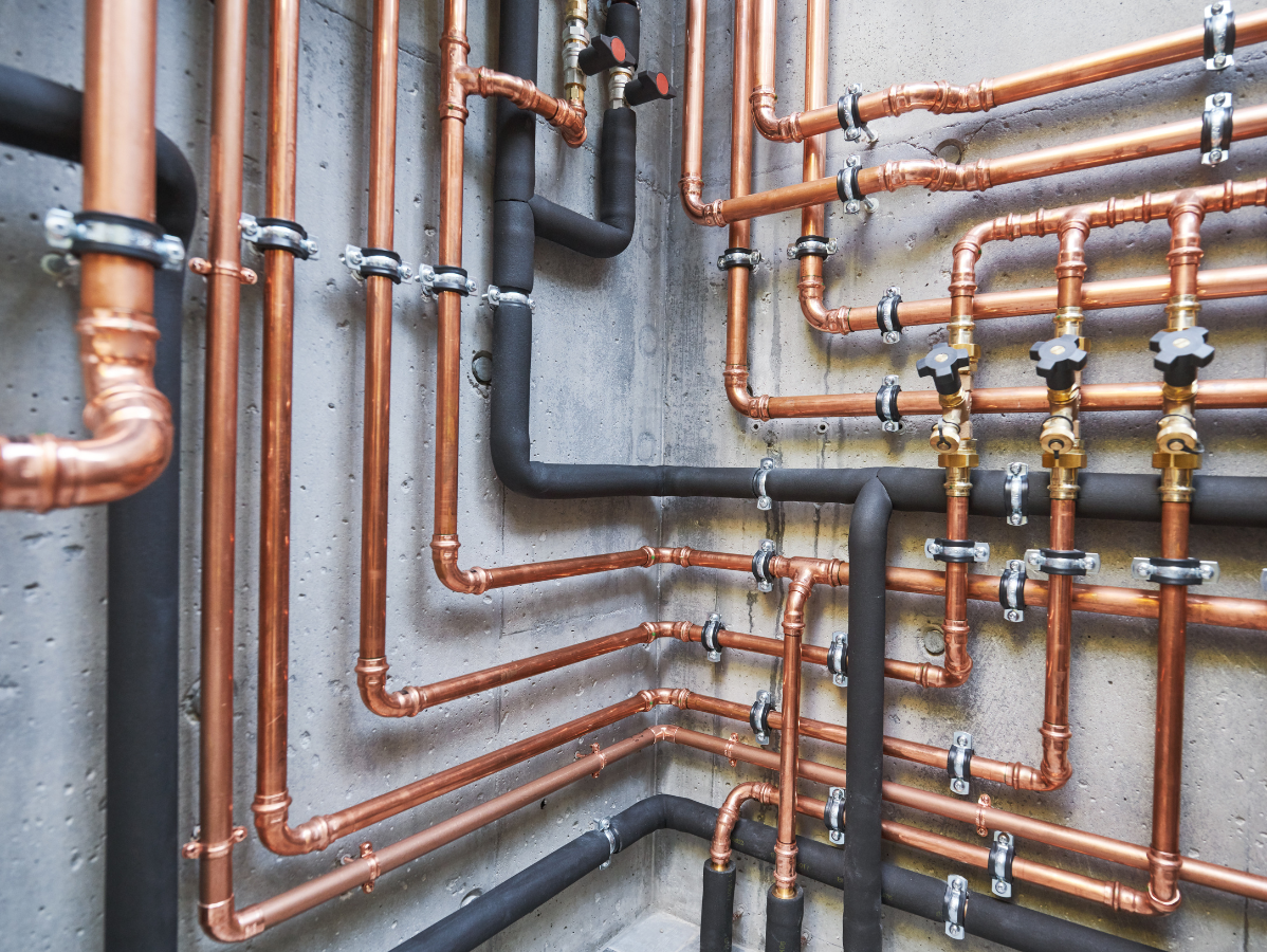 Copper and black pipes with valves against a concrete wall.
