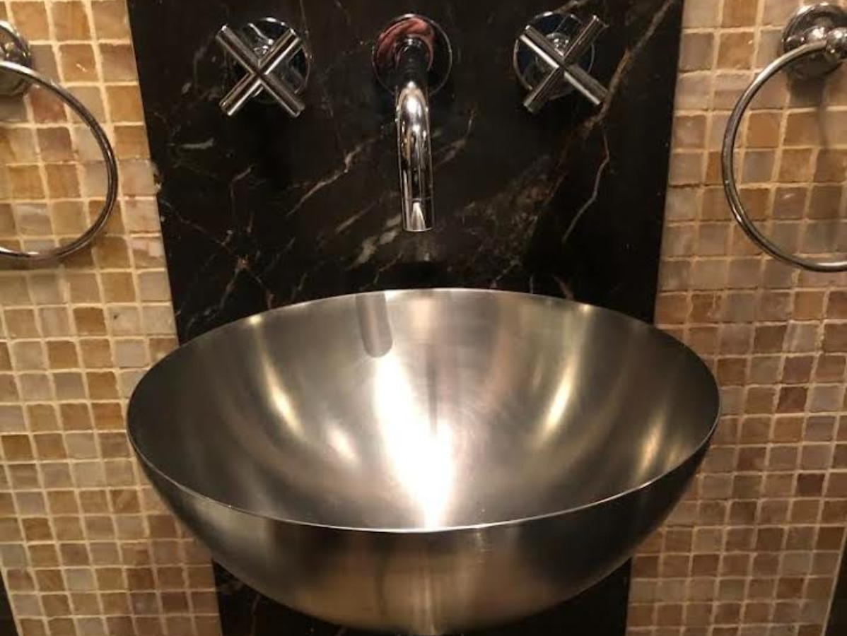 Stainless steel bowl sink with chrome fixtures set against black marble and mosaic tile.