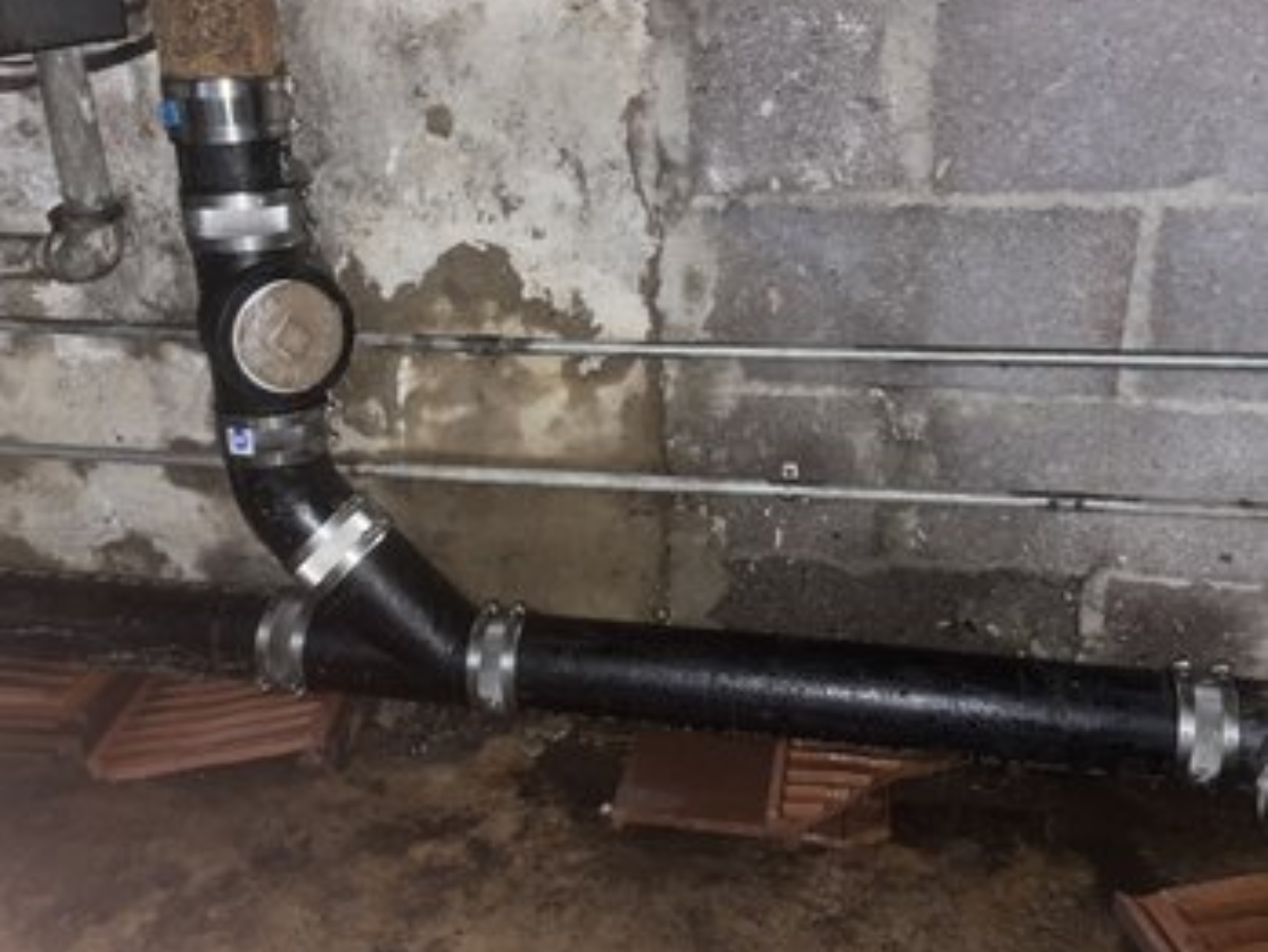 Black plumbing pipes against a gray cinder block wall in a basement.