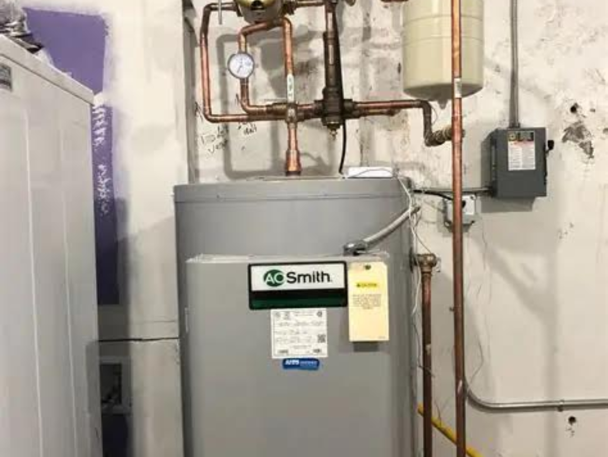 Water heater with copper pipes against a concrete wall. A gray control box is also visible.