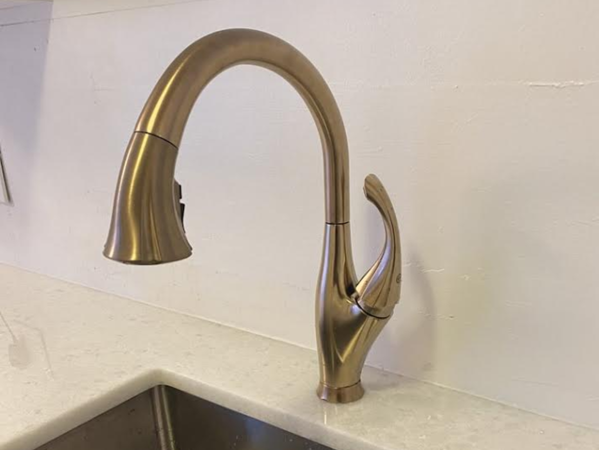 Bronze kitchen faucet over a stainless steel sink, against white backsplash and countertop.