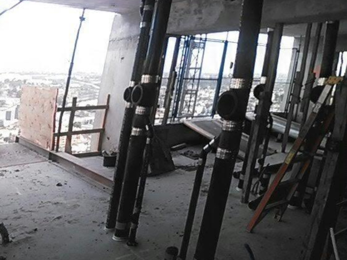 Construction site interior: black pipes installed inside building under construction, cityscape in background.