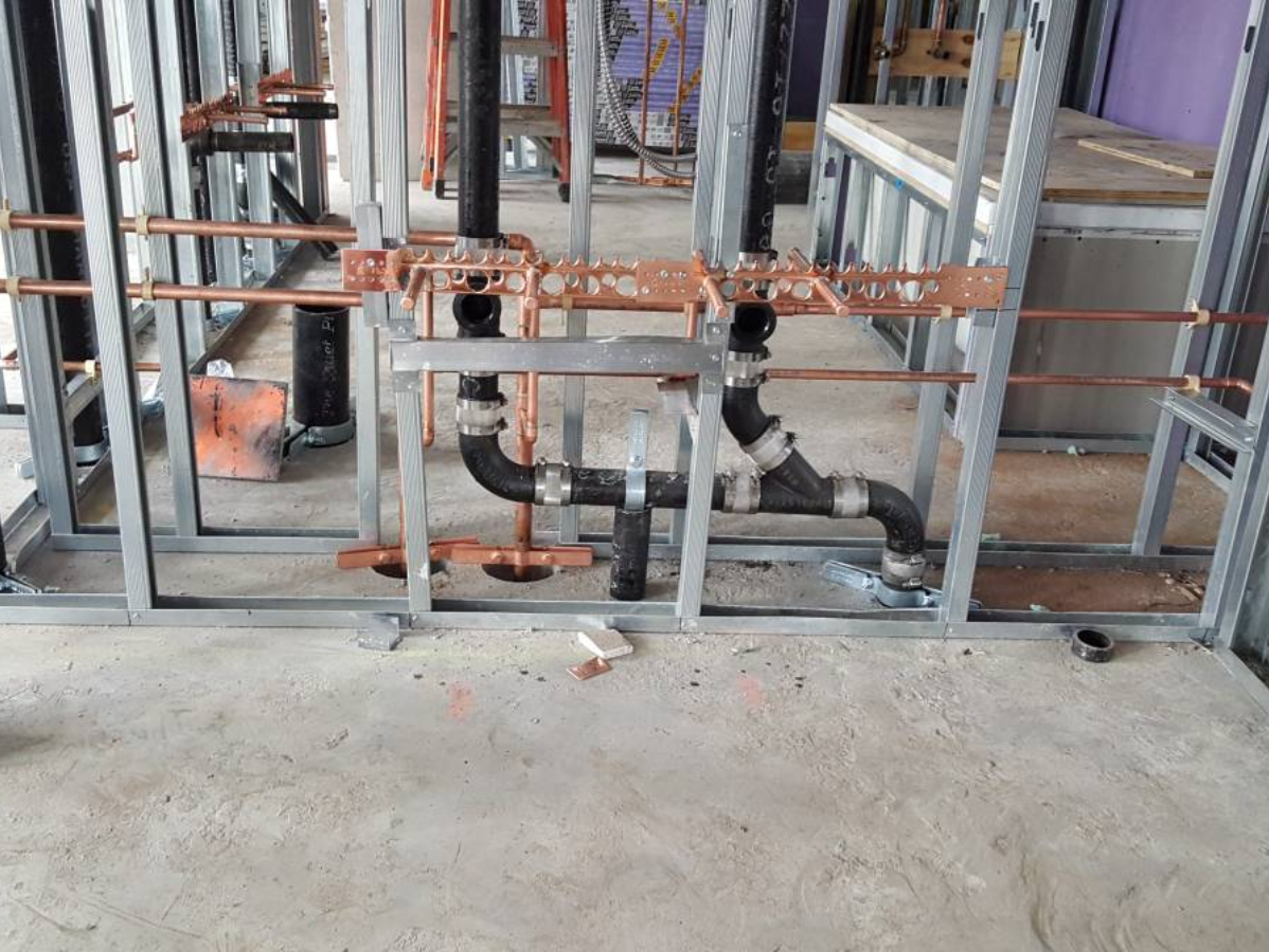 Plumbing in construction: copper pipes and black drain pipes installed within metal framing.