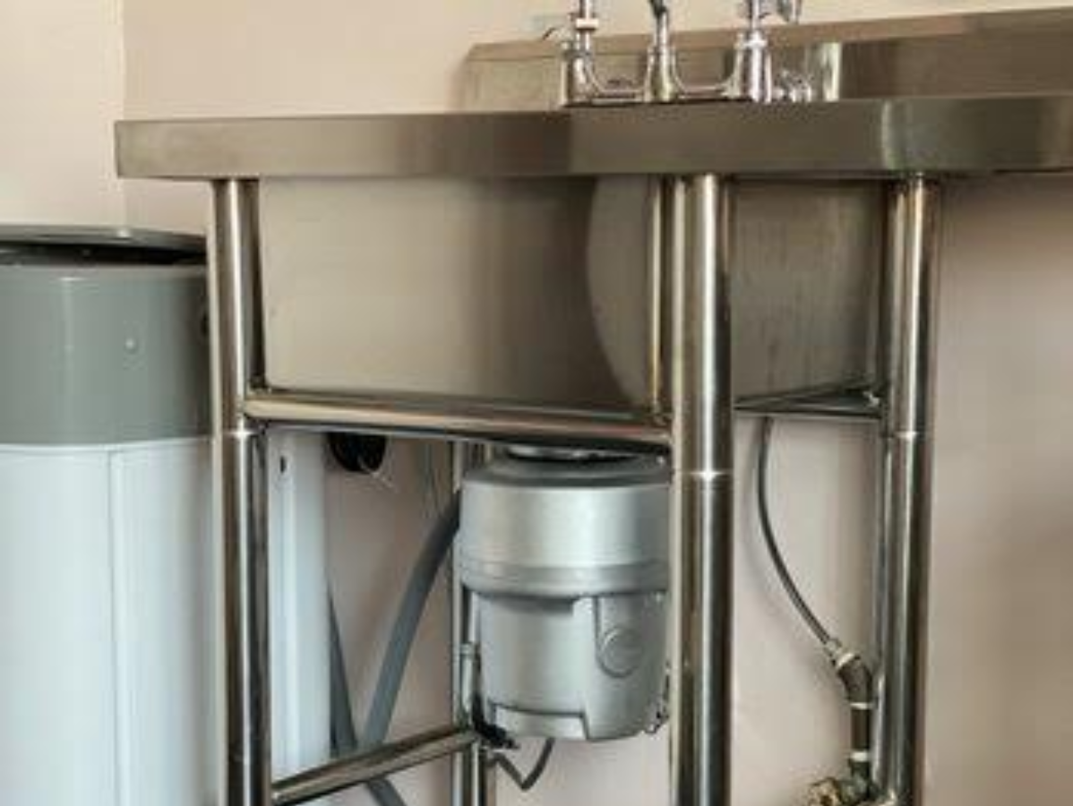 Stainless steel sink with exposed plumbing, garbage disposal, and adjacent water heater.