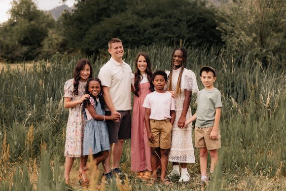 Family of six standing together in a grassy field, smiling at the camera.