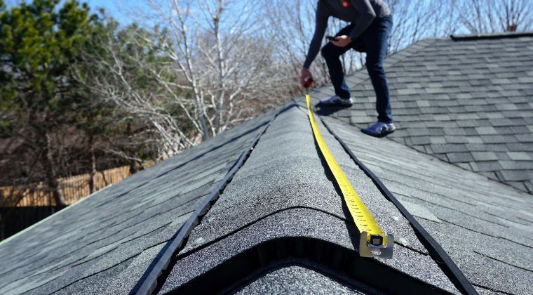 A man is measuring a roof with a tape measure.