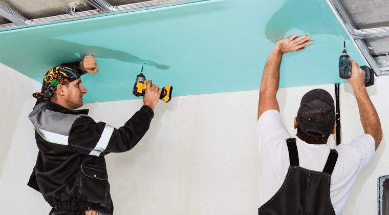 Two men are working on a ceiling in a room.