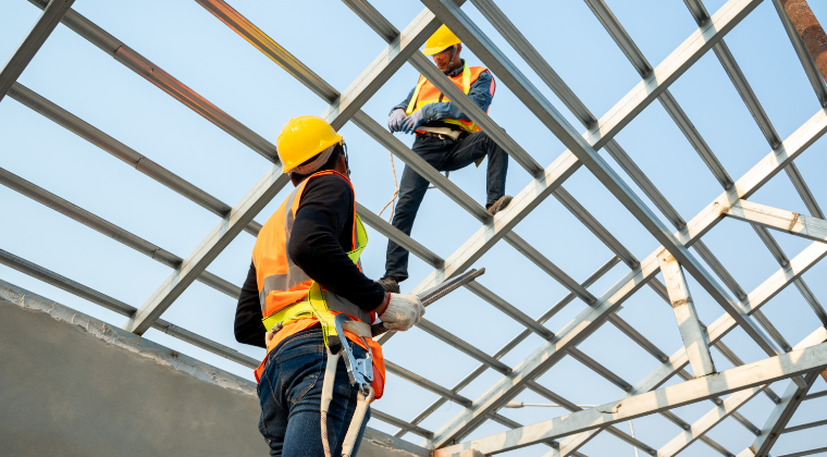 Two construction workers are working on a metal structure.