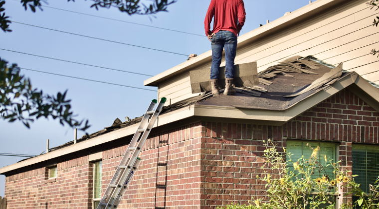 A man is standing on the roof of a house with a ladder.