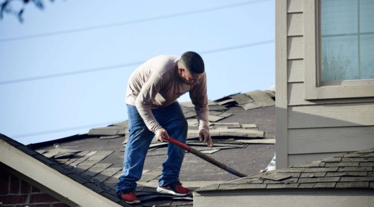 A man is standing on top of a roof holding a rake.