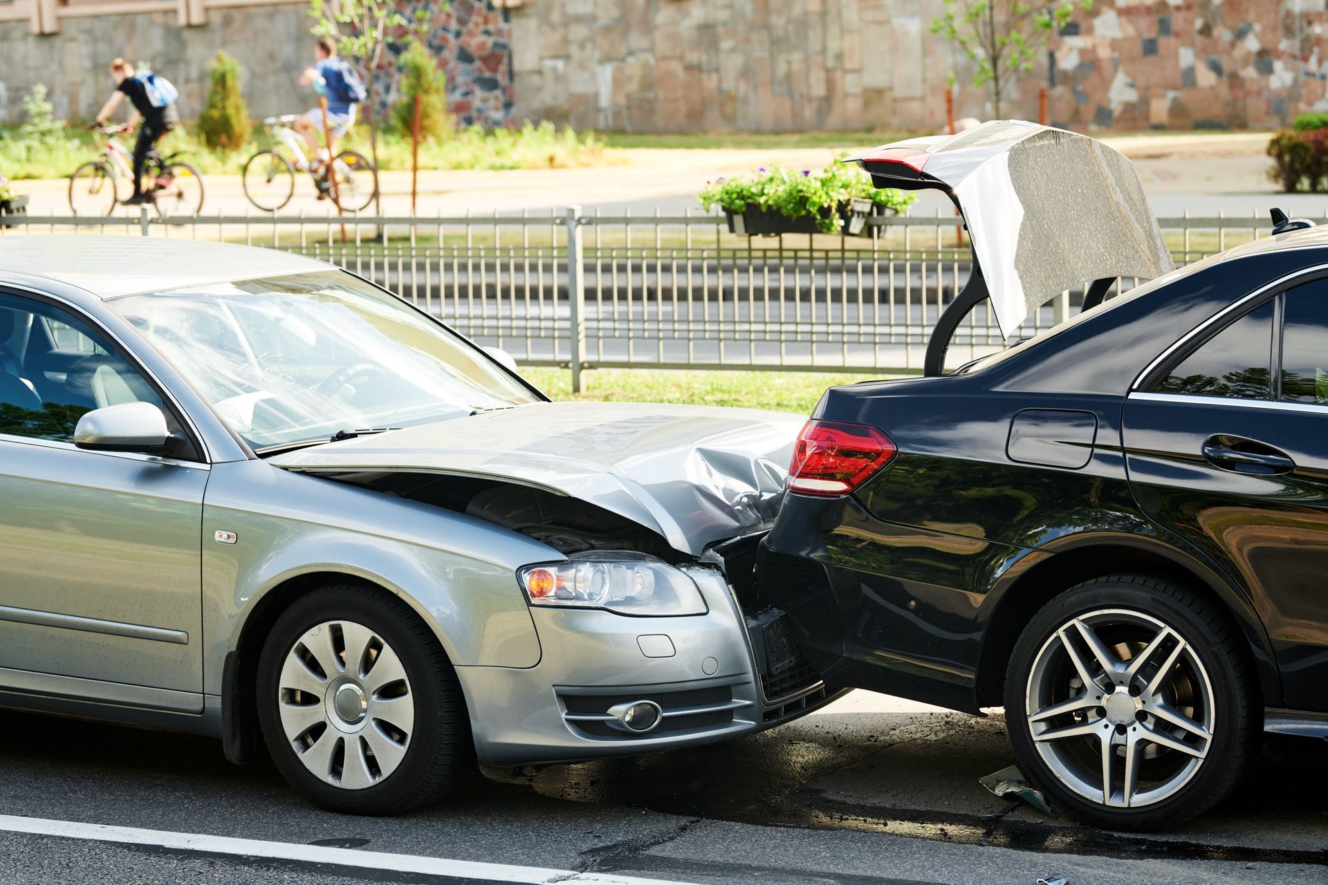 Two cars, one silver and one black, damaged in a collision on a street.