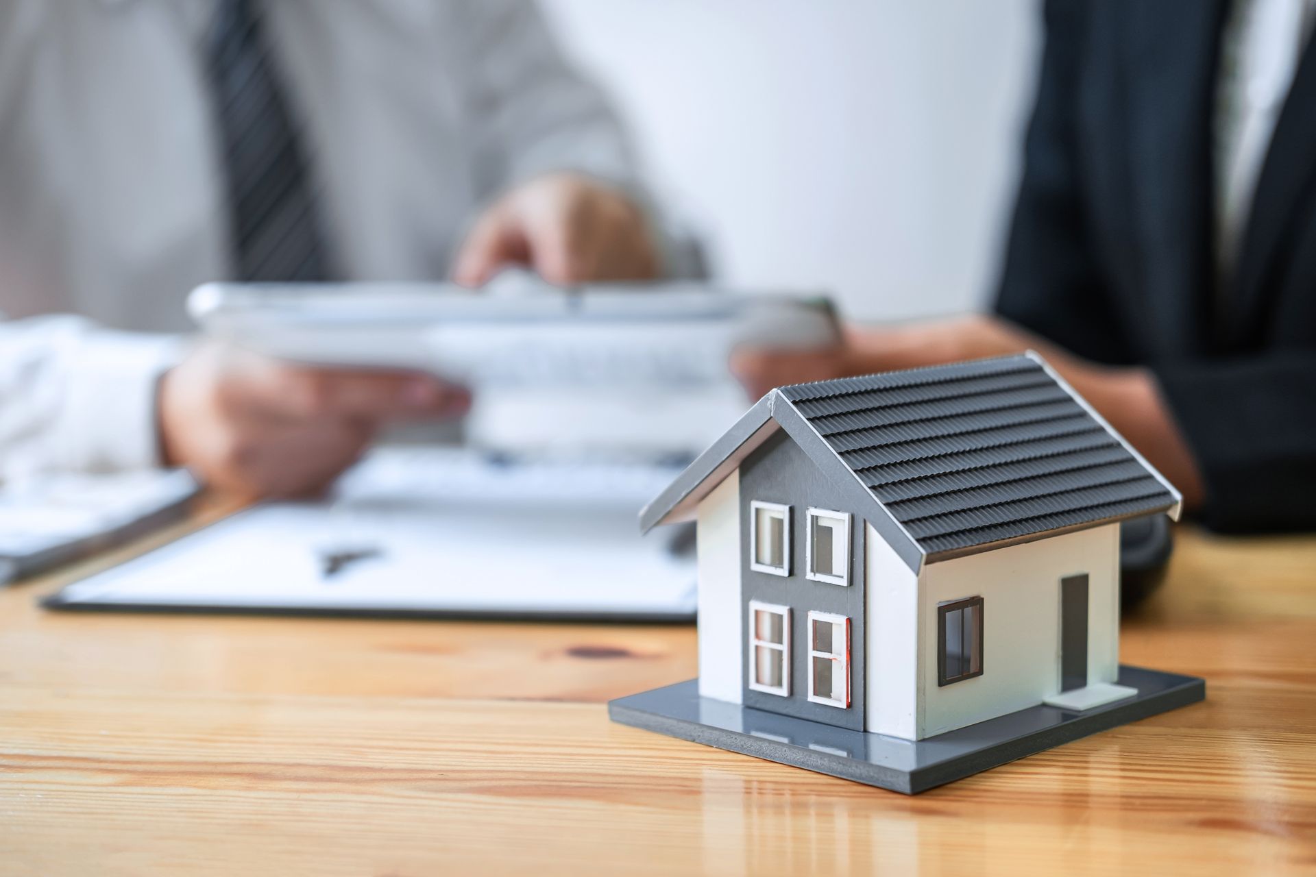 Toy house in front of people discussing paperwork on a wooden table.