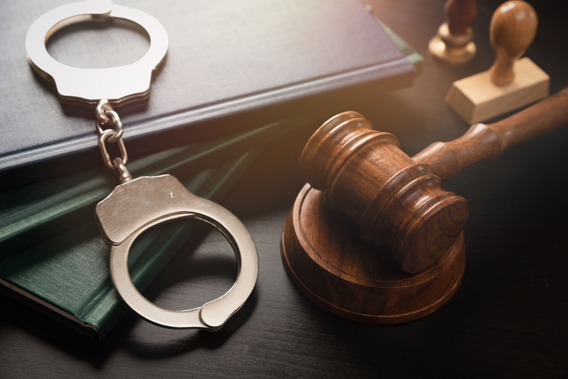 Handcuffs, gavel, and legal book on a dark surface, representing law and justice.