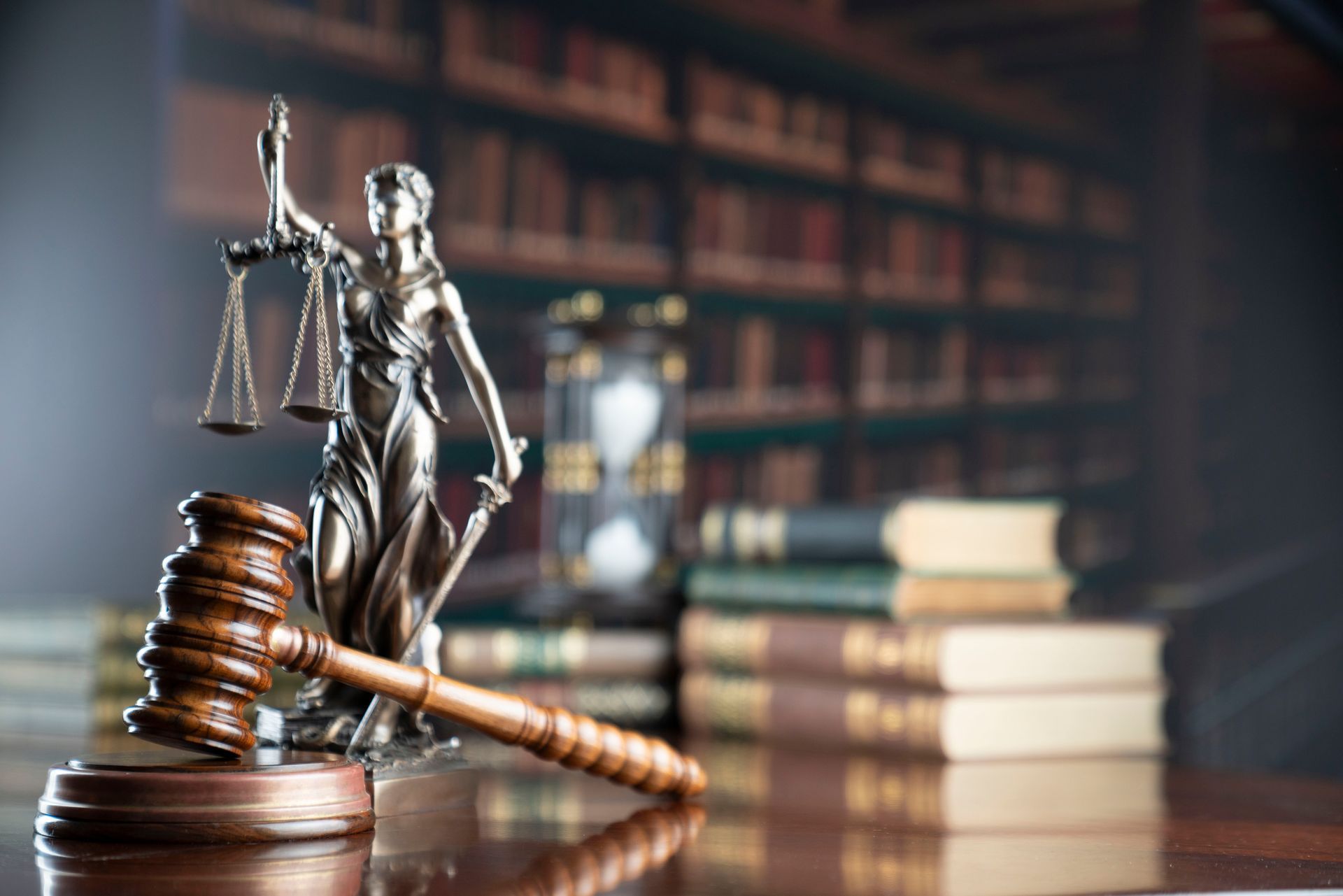 Gavel and Lady Justice statue on desk, books in background.
