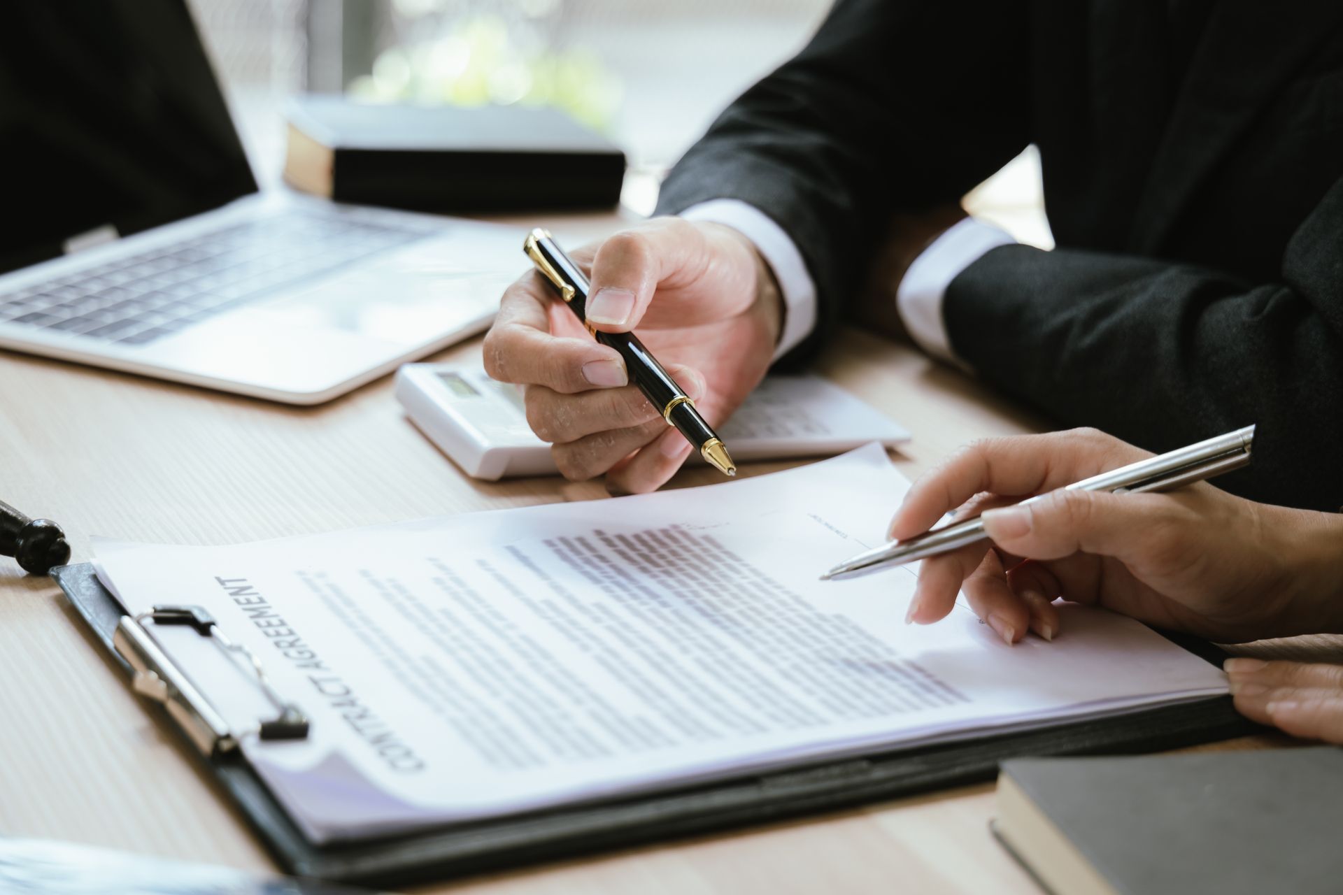 Two people reviewing a contract, hands pointing to text with pens, office setting.