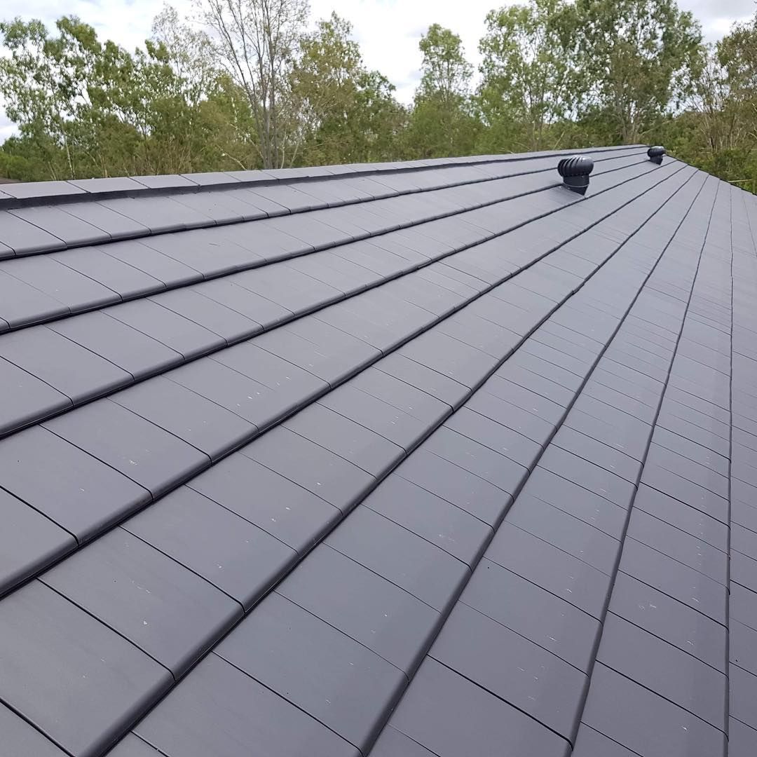 A close up of a black roof with trees in the background.